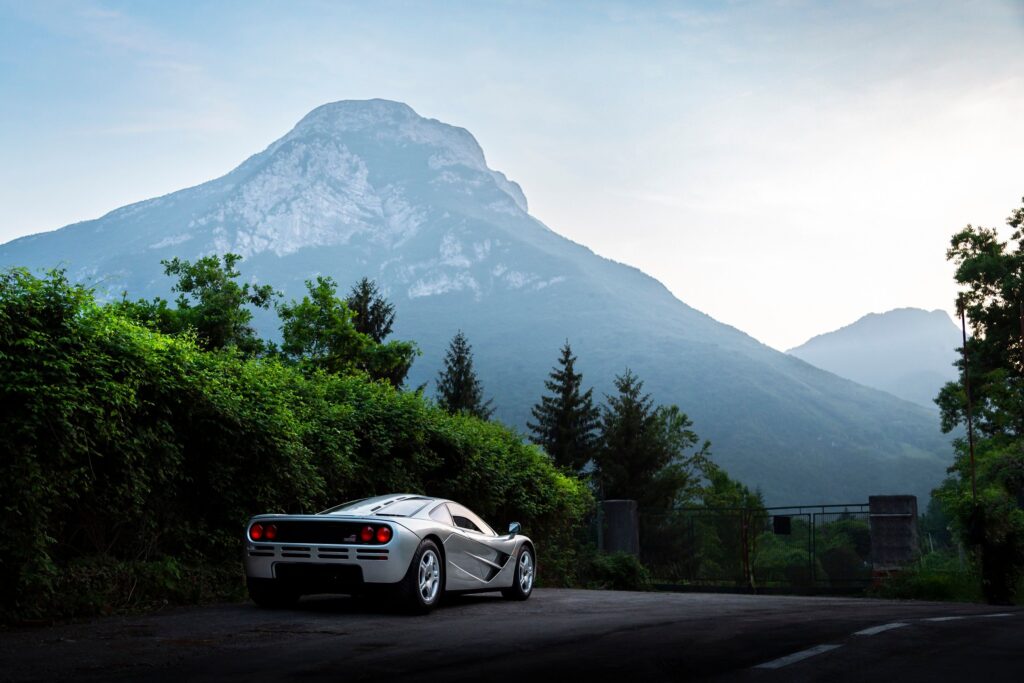 A classic supercar parked in front of a scenic mountainous landscape during the day.