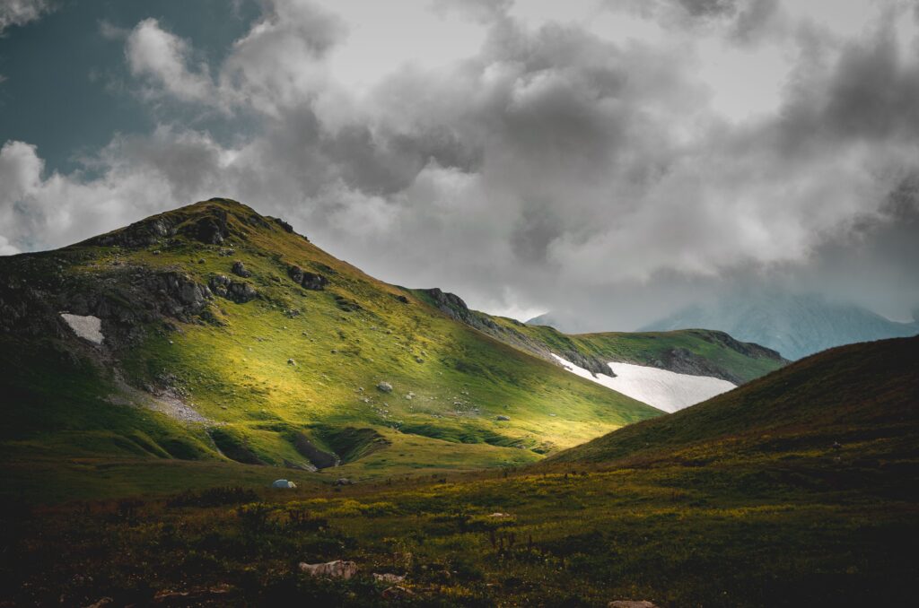 A breathtaking mountain landscape with vibrant green hills and a dramatic clouded sky.